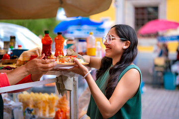 Joyful young Latina woman receiving traditional Mexican chicharrón preparado at street food stand in Centro de Coyoacán, Mexico City
