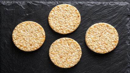 Overhead view of four round sesame seed cakes on a dark textured surface