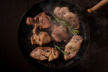 Several pieces of cooked beef steak sizzling in a black cast iron skillet