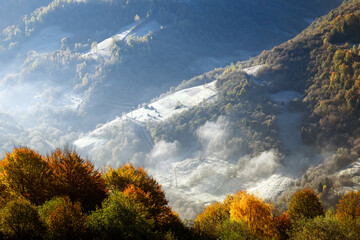 Rural scene with frosty hills with fog flowing over freeze pasture with house and haystacks in...