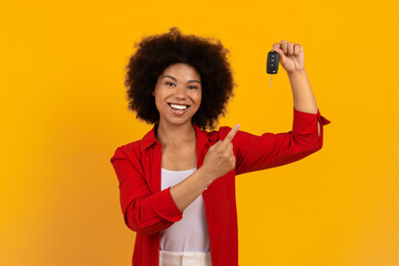 Smiling African American woman in red outfit proudly pointing to car key. New car ownership or...