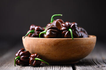 Ripened chocolate habanero peppers (capsicum chinense) in wooden bowl on rustic table. Very hot mexican peppers close up