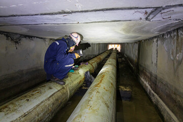 Male worker inspection of rusted steel pipe, underground steel deterioration, widespread corrosion, and confined spaces