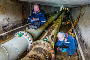 Male worker inspection of rusted steel pipe, underground steel deterioration, widespread corrosion, and confined spaces