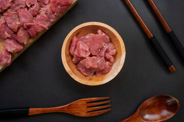 flat lay of raw meat in a wooden bowl and wooden tray on black background
