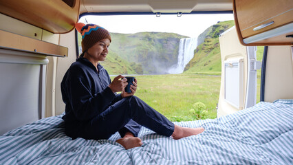Relaxing with a warm drink in a camper van by a stunning Icelandic Skogafoss waterfall