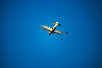 A skydiver on a multi-colored rainbow parachute jumps out of an airplane in a blue clear sky	
