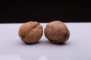 Two walnuts rest on a white surface