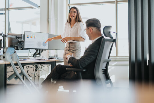 A diverse team of business employees discussing project results in a bright office space. A woman presents data on a screen to colleagues, fostering teamwork and collaboration.