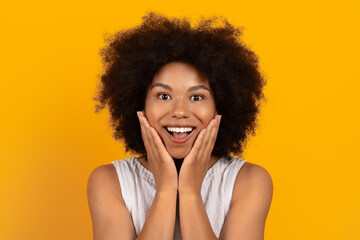Surprised and delighted young black woman touching face with hands. Positive emotion, excitement...