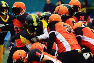 American football players in black and yellow uniforms fight for the ball with players in black and...