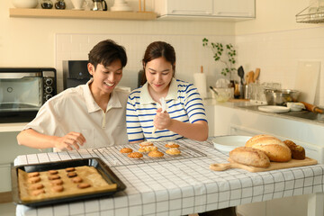 Happy duo decorating baked cookies on a wire rack with icing, perfect for home baking, food preparation, and family activities