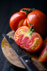 Large juicy tomatoes sliced on round wooden cutting board. Old knife and rustic wooden table. Top view food photography