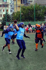 American football players in orange - black uniform and a player in blue - black uniform play on the green field at the stadium	
