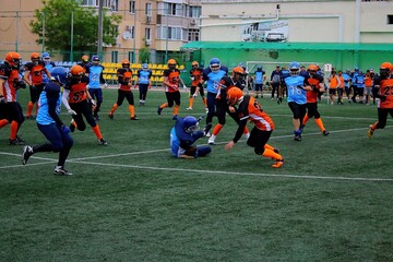 American football players in black and orange uniforms play with players in blue and black uniforms...