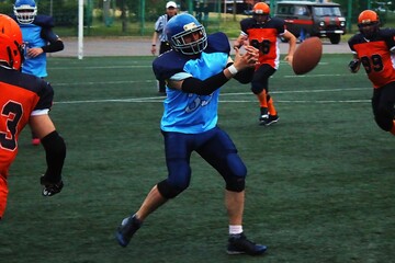 American football player in black and blue uniform catches an oval ball	
