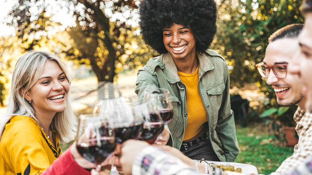 Happy friends having bbq dinner party in garden restaurant - Multiracial young people eating grill meat and drinking red wine in backyard - Food life style concept with guys and girls sitting outdoors