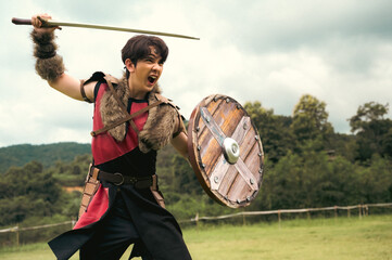 Aggressive handsome Viking worrier man holding sword and shield ready to fight in battle field
