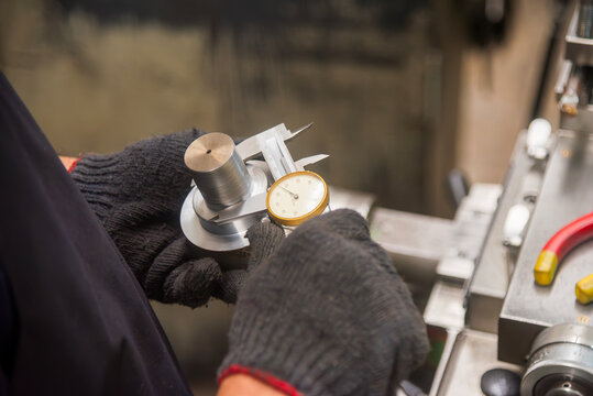 Close up scene the machine operator measuring dimension of metal shaft parts by dial Vernier caliper.