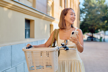 Asian woman walking in the city with her bicycle while using a smartphone app for sharing transport