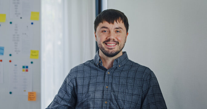 Portrait confident smiling male programmer working with robotics code AI software and looking at camera in tech office. Artificial intelligence dashboard, robotics, user interface, machine learning.
