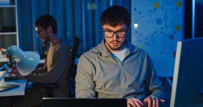 Team adult male freelance developer work late typing write prompt AI bot app program nomad terminal code at office night. Artificial intelligence dashboard, robotics, user interface, machine learning.