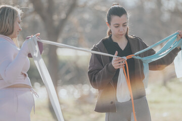 Two women engage in a fitness activity outdoors holding colorful resistance bands, set in a sunlit...