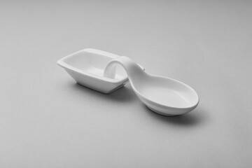 A white ceramic spoon rest sits on a light gray surface