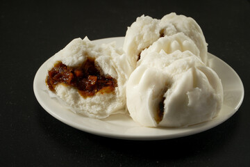 Chinese steamed bun with bbq pork filling on a white plate and black background
