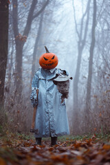 Creepy figure with pumpkin mask and axe weapon stands in misty autumn forest with severed scarecrow head. Dark Halloween concept filled with forest horror and chilling tension