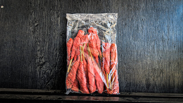 various frozen foods - various fried foods in sealed plastic packaging - kribo is a pink satay-shaped fried food wrapped around a wooden stick
