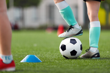 A close-up of a young soccer player in soccer socks and cleats with black and white soccer ball on...