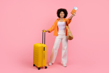 Joyful young black woman holding passport and travel tickets while standing with suitcase. Ready...