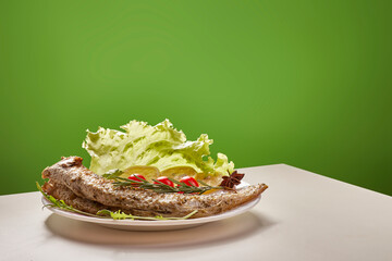 A grilled fish rests on a white plate, garnished with fresh lettuce, red chili peppers, and star...