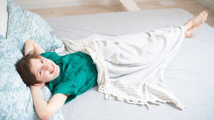 happy boy in green pajamas is lying on bed in bedroom