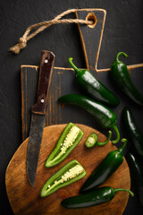 Black jalapeno hot peppers on wooden cutting board with rustic knife close up. Food photography