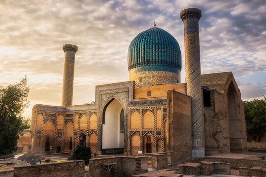 View of the Gur-e-Amir Mausoleum stands majestically with its fluted azure dome and tall minarets against a golden sky, Samarkand, Samarqand Region, Uzbekistan.