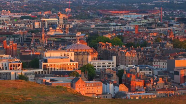 Aerial video reveal of Edinburgh Cityscape in Scotland touched by the golden light of Sunrise from the cliffs of Holyrood Park