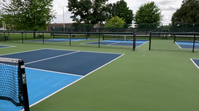 Outdoor Pickleball Courts. Sweeping views in motion of empty pickleball courts. Moving forward across several courts in a row. Public city park setting with cloudy blue Summer sky.