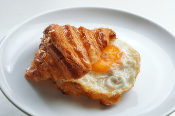 Crunchy croissant sandwich with a fried egg on a white plate.