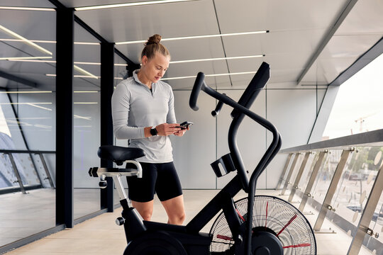 Woman using smartphone beside exercise bike in a modern gym setting