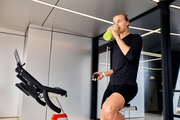Woman drinking water while exercising on a stationary bike indoors