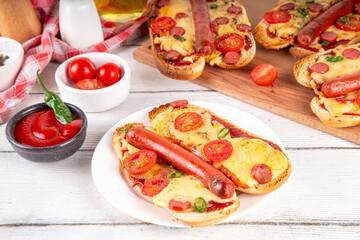 Tasty gourmet pizza dogs trendy viral combination recipe of hot dogs with hot sausage and pizza with tomatoes, cheese, jalapeno peppers, cherry tomatoes and herbs, with sauce on white wooden table