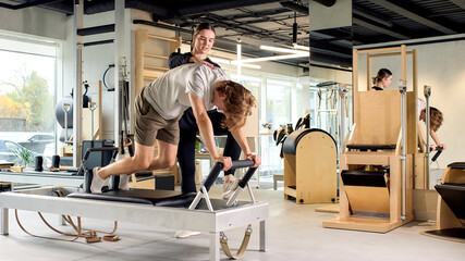 Personal trainer guiding male client during a reformer Pilates session in a studio