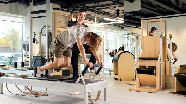 Personal trainer guiding male client during a reformer Pilates session in a studio