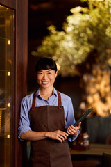 Smiling Female Restaurant Worker in Uniform Holding a Clipboard at the Workplace