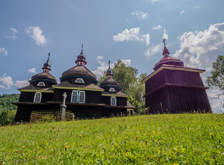 Wooden church and bell tower in Nizny Komarnik, Slovakia. Peaceful rural scene with grass, cross...