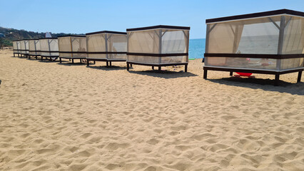Obraz premium Beach scene with several white cabanas on golden sand. Clear blue sky and calm ocean in the background. Ideal for relaxation and vacation concepts.