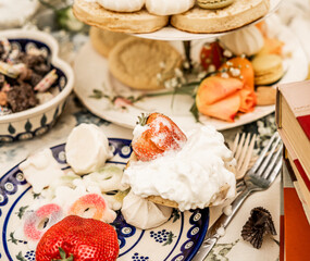 whipped cream dessert with a whole strawberry, surrounded by sweets on messy table
