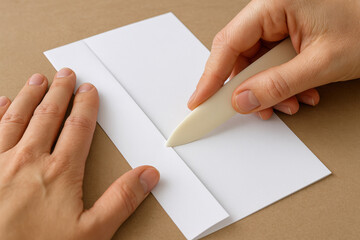 Obraz premium Paper Folding: A person's hands expertly fold crisp, white paper using a bone folder, perfect for crafting and detailed work.